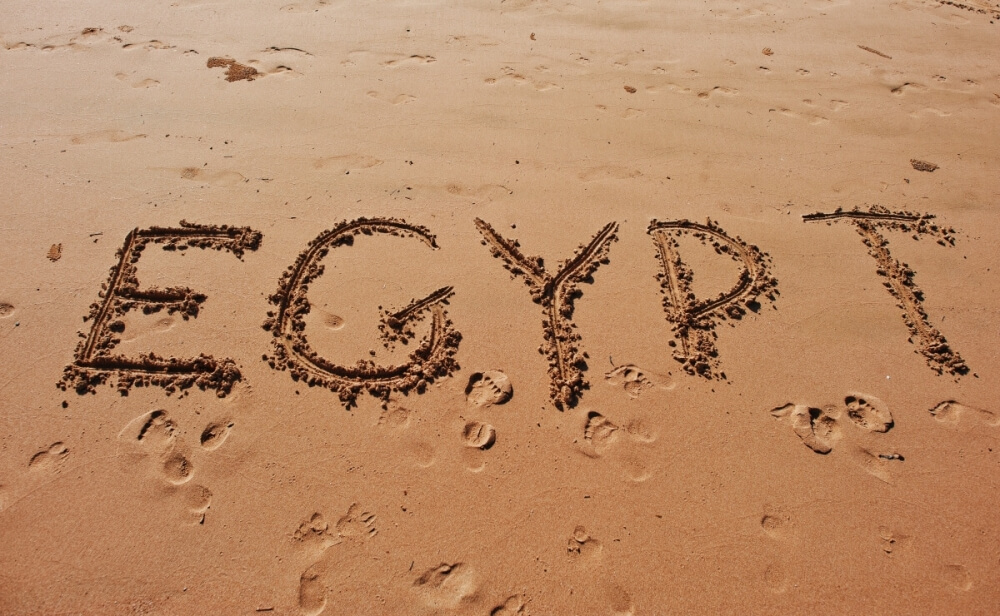 Napis "EGYPT" wypisany na piasku pustyni ze śladami stóp wokół